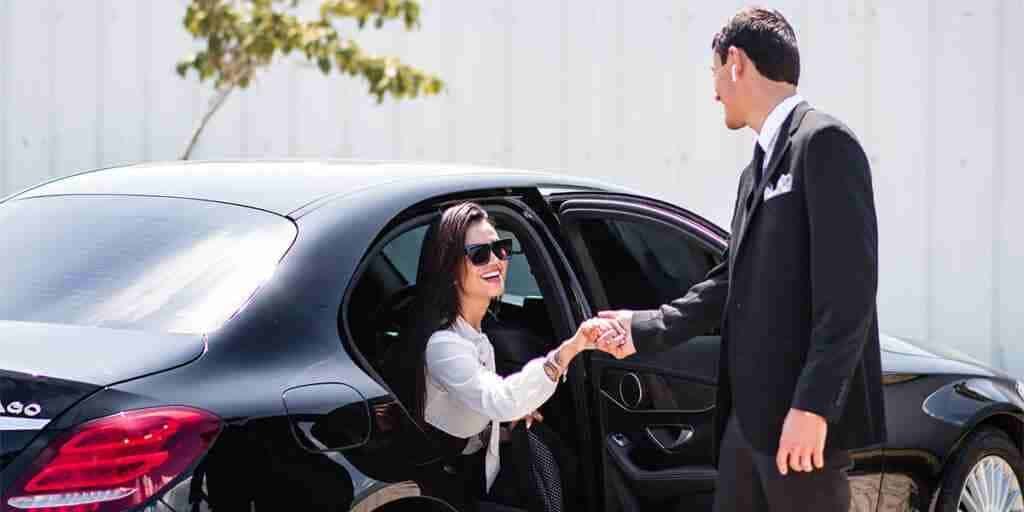 Rio de Janeiro limo service featuring a sleek black car, a passenger in a white shirt and sunglasses, greeted by a professional chauffeur
