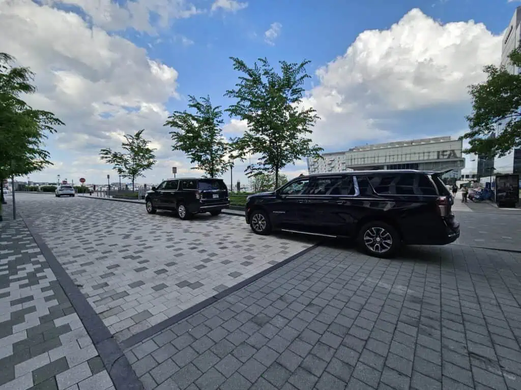Two black Chevrolet Suburban SUVs from the Boston Luxury Chauffeur fleet parked on a Boston waterfront promenade