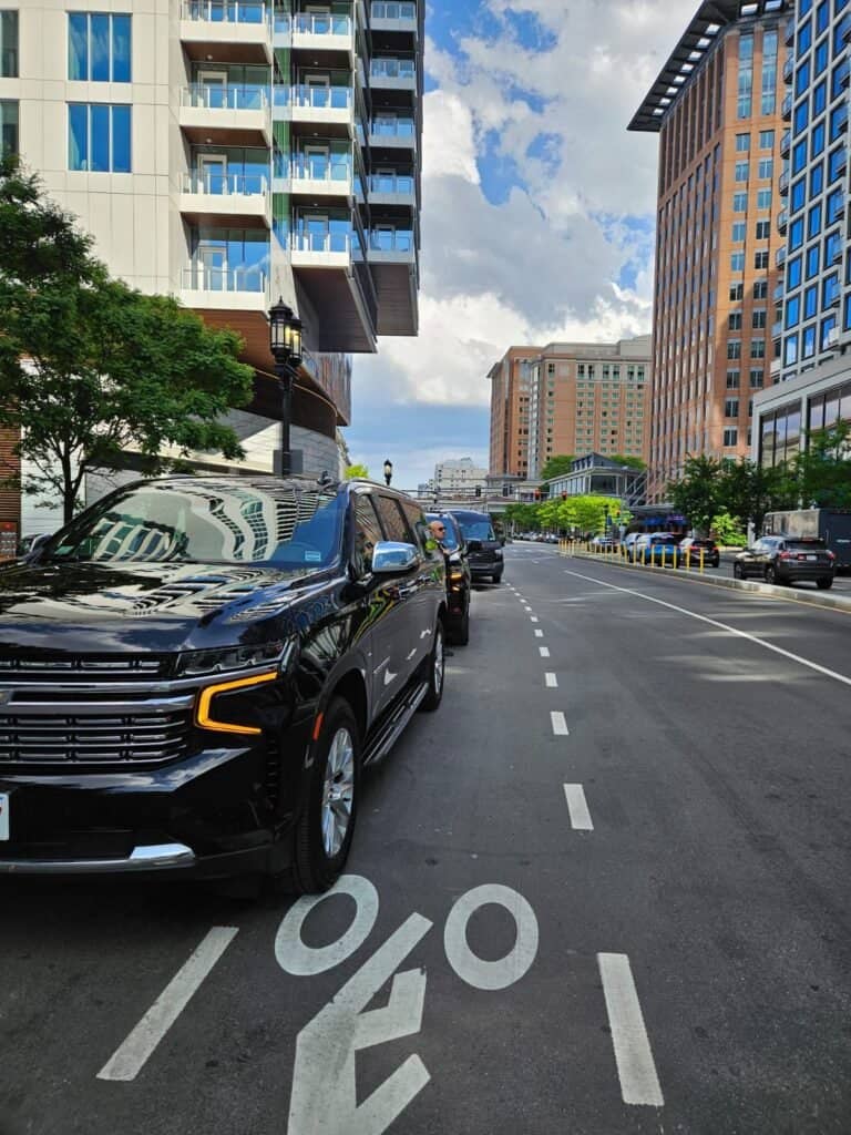 Boston Luxury Chauffeur black Chevrolet Suburbans lined up along a city street beside high-rise buildings