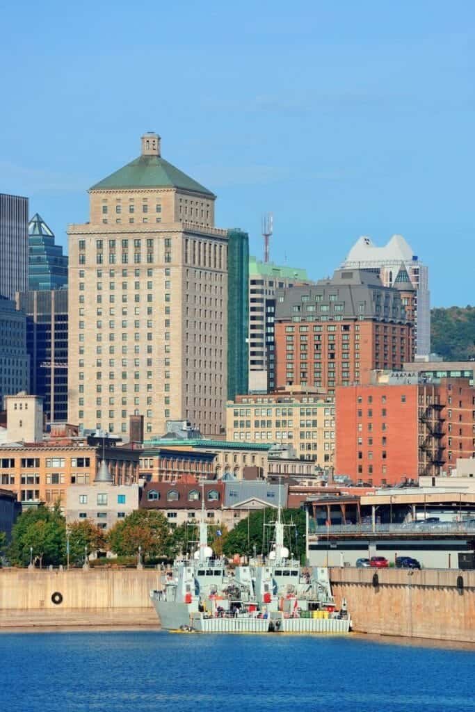 Montreal skyline across the river featuring a beige stone high-rise with a green roof, surrounding colorful buildings and a calm blue waterfront under a clear sky