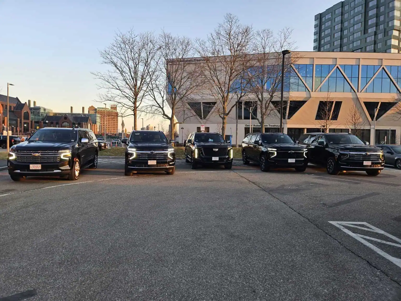 Boston Luxury Chauffeur fleet of black Chevrolet Suburbans lined up in front of a modern building at sunset