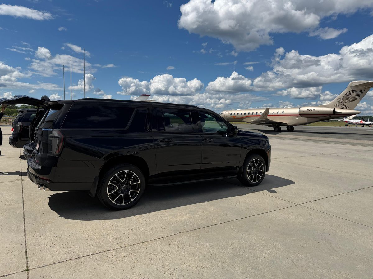 Black Chevrolet Suburban RST luxury SUV parked beside private jet on tarmac at Hanscom Field — Boston Luxury Chauffeur private aviation ground transportation